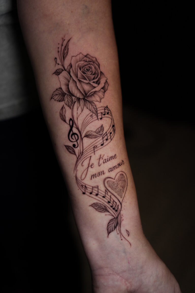 Erinnerungs-Tattoo am Unterarm mit Rose, Notenlinien, Schriftzug Je t'aime mon amour und Herz mit Fingerabdruck, gestochen von Mykhailo im Amy's Aesthetic Atelier